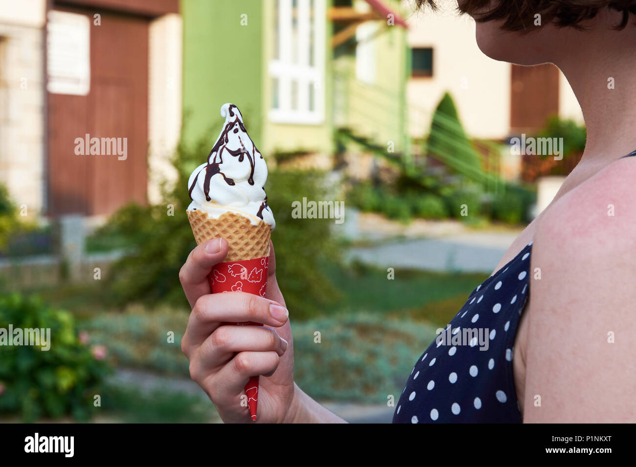 Young woman holding ice cream in hands, with houses, town and trees blurred in the background Stock Photo