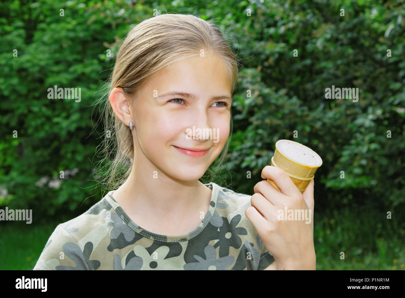 A cute 13 year old girl with ice cream in her hand walking in summer park. The joy of the holidays Stock Photo