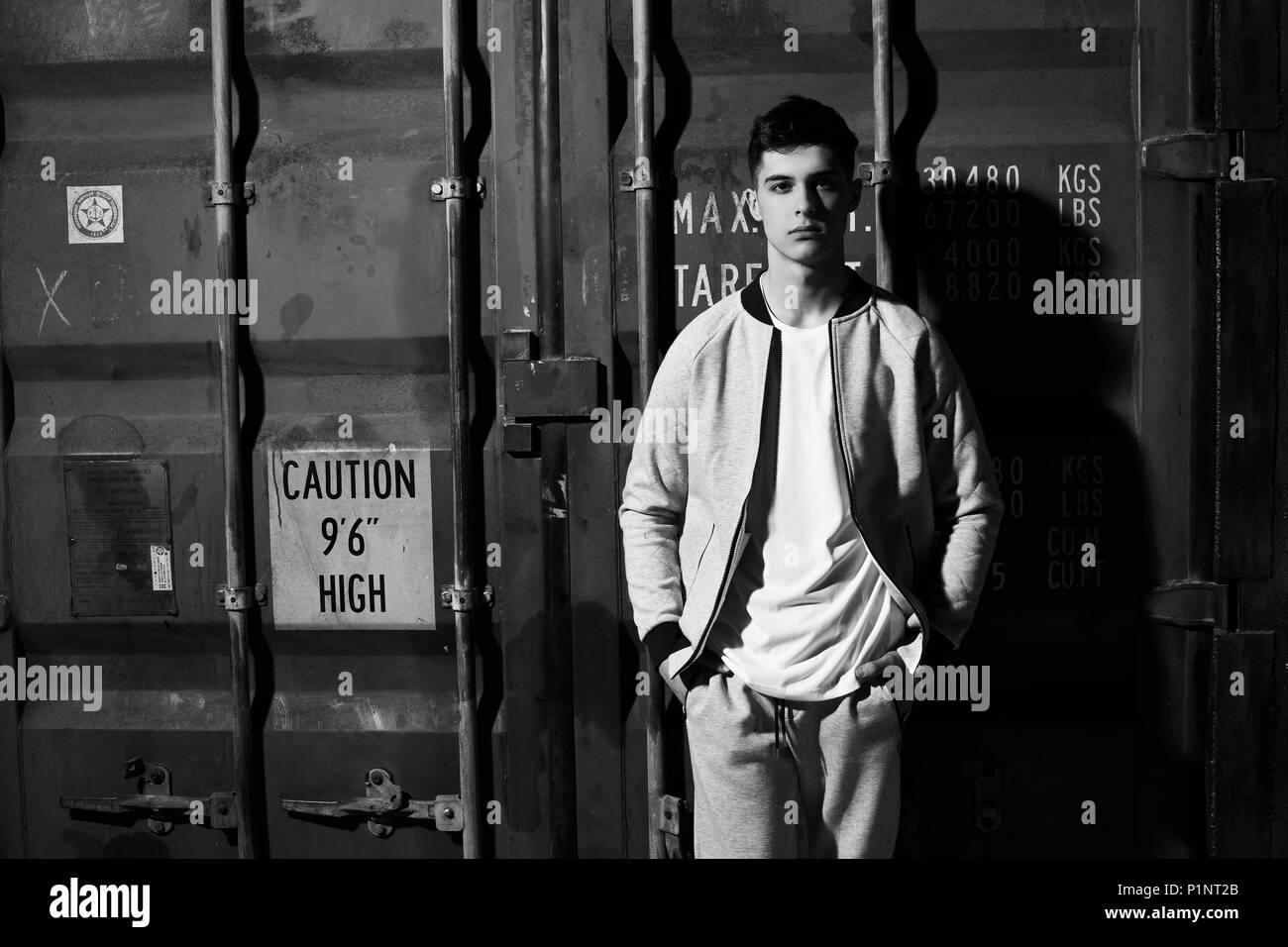 Young handsome sporty man in gary sport clothes posing against red metal doors of intermodal container Stock Photo