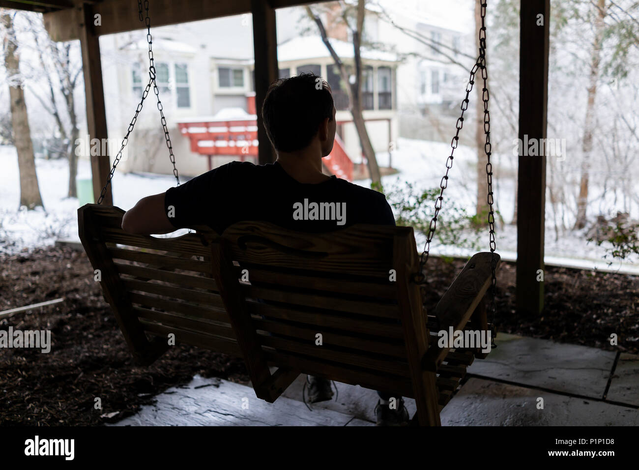 Man Sitting Swinging On Swing Under Wooden Deck Of House On
