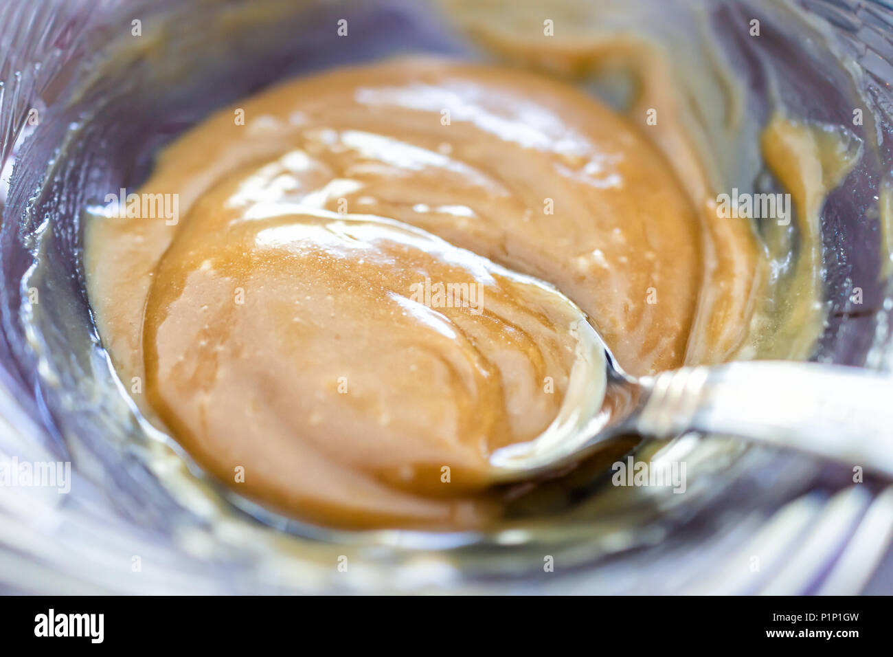 Macro closeup of golden brown caramel sauce with spoon thick gooey