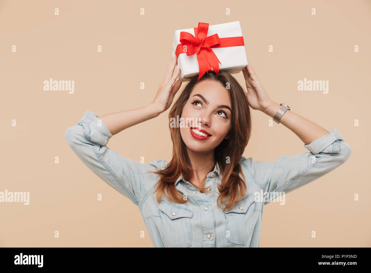 Portrait of a happy young girl holding present box on her head isolated ...