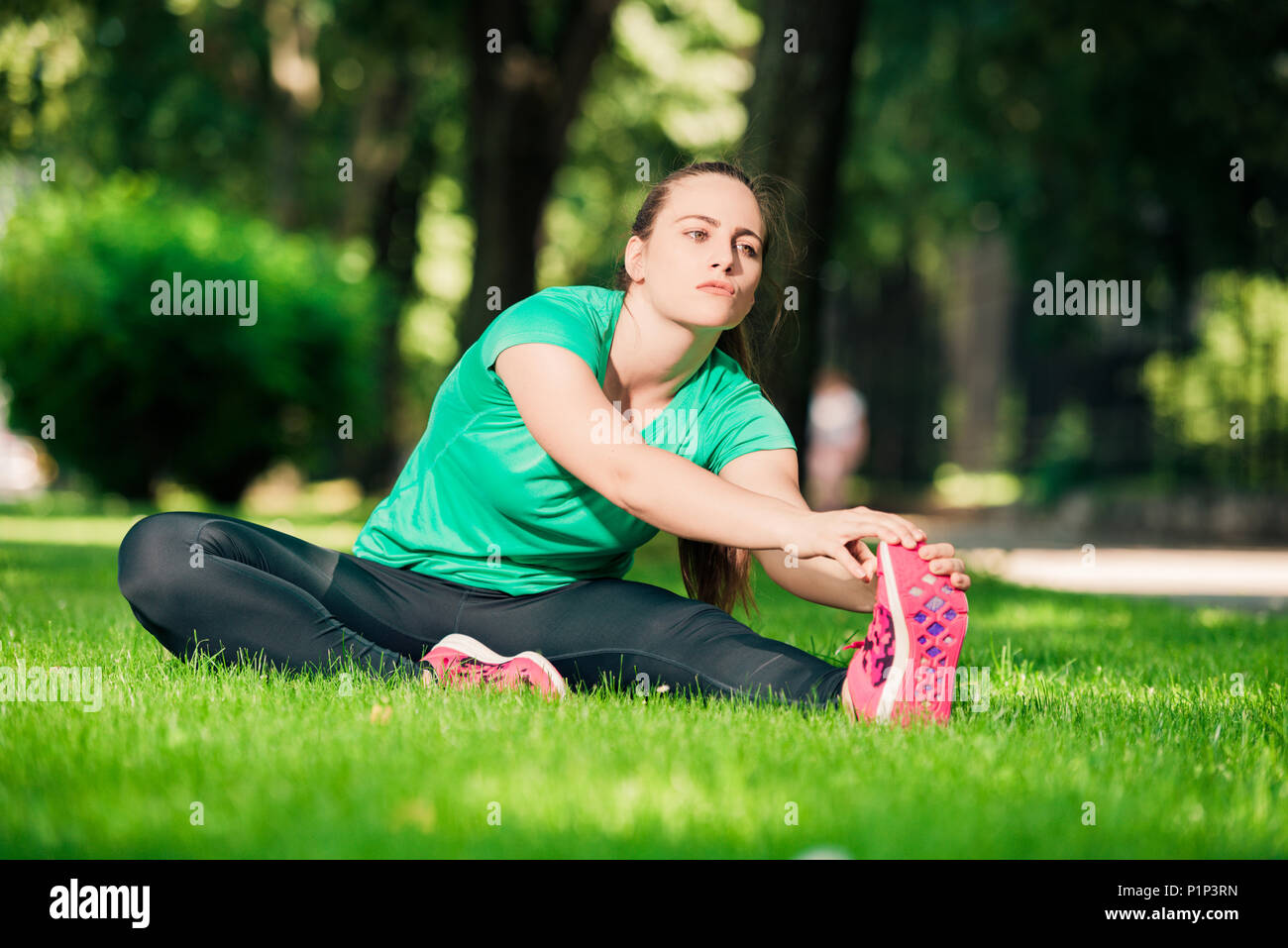 Young pretty woman sitting on the grass and stretching her legs Stock ...