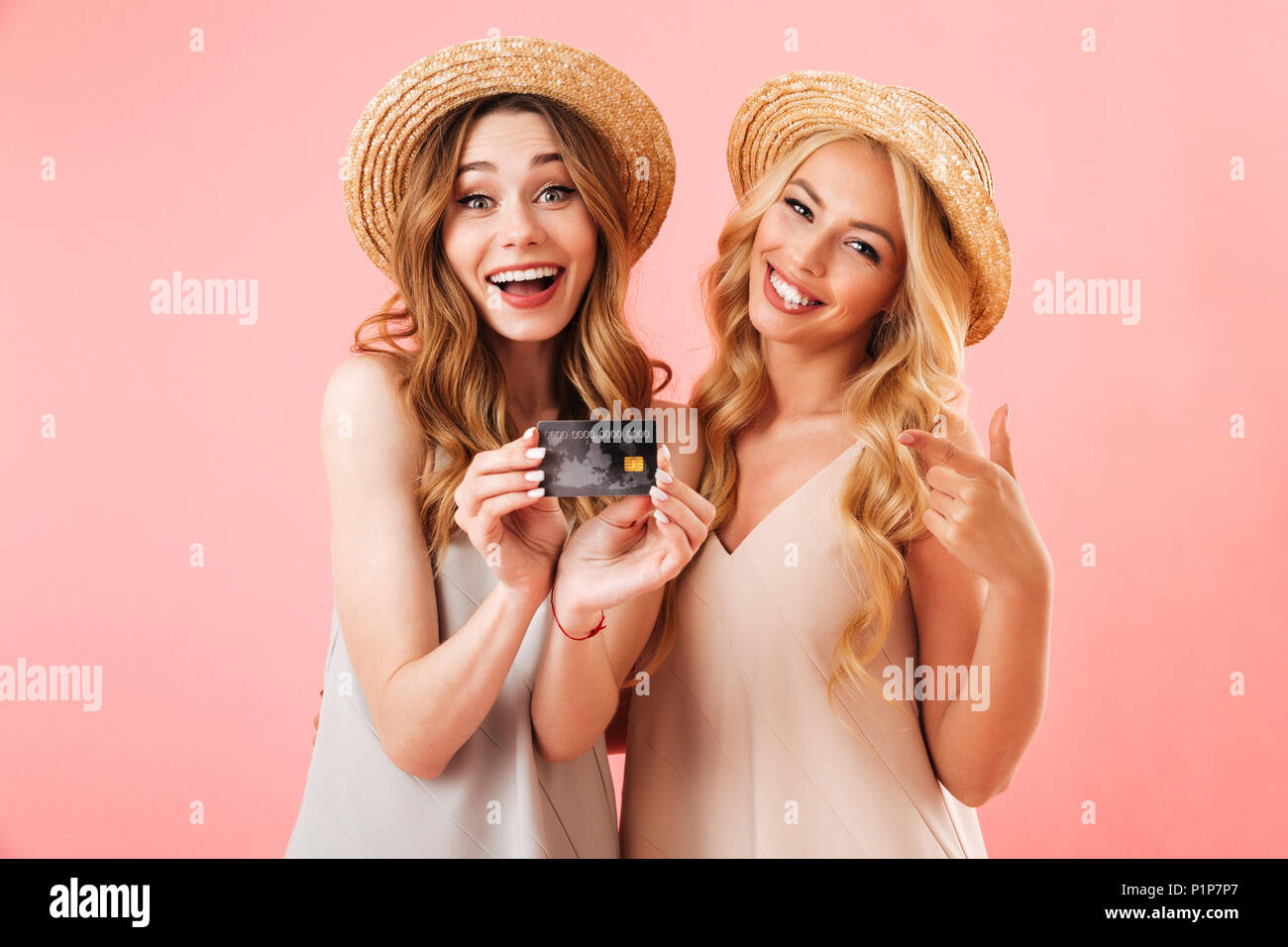 Portrait of two happy young women in summer clothes showing plastic credit card isolated over pink background Stock Photo