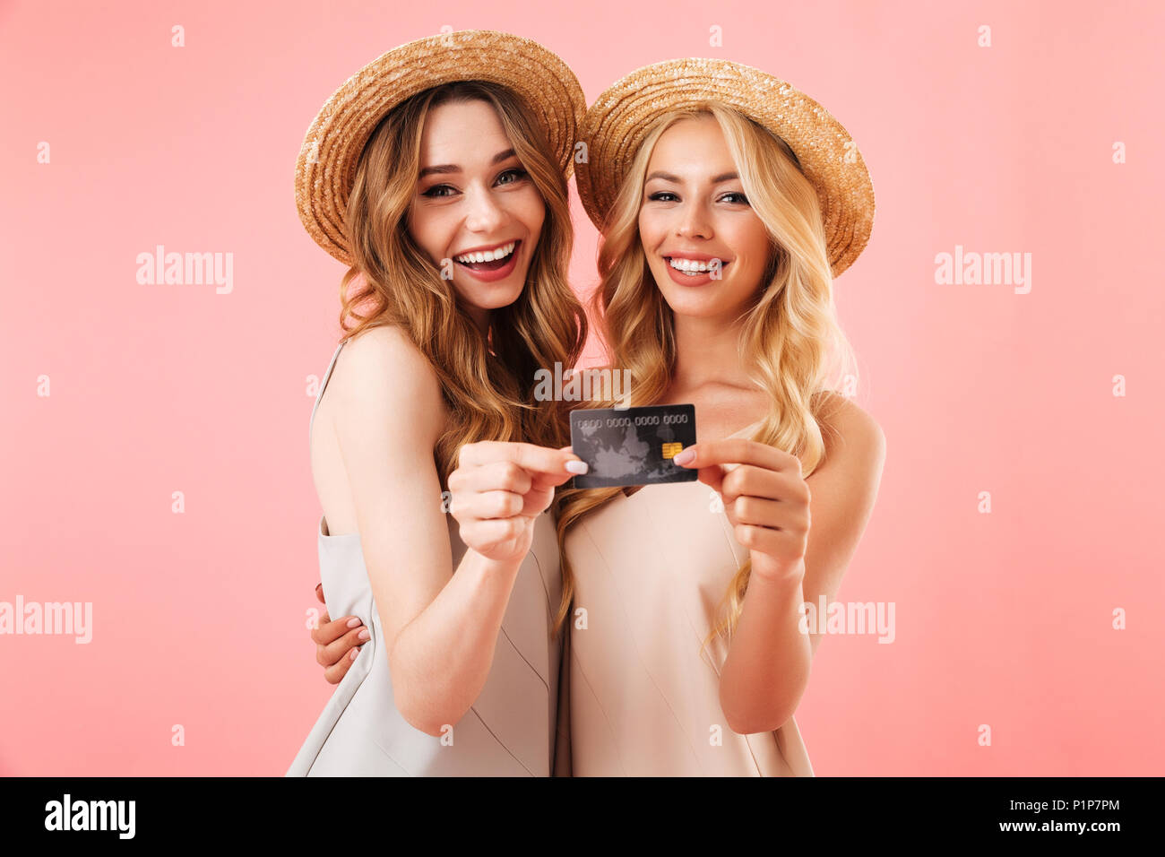 Portrait of two smiling young women in summer clothes showing plastic credit card isolated over pink background Stock Photo