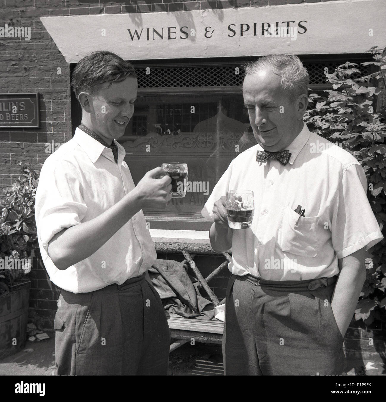 1955, cheers! historical picture, two gentlemen, the younger one wearing a cravat, the older one, a bow tie, stand outside a pub having a drink together, a tankard of Fremlin's beer or ale, Whitstable, Kent, England, UK. Stock Photo