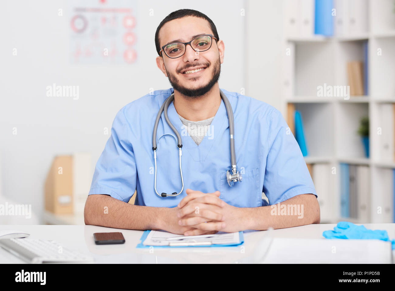Cheerful Middle-Eastern Doctor Posing at Desk Stock Photo