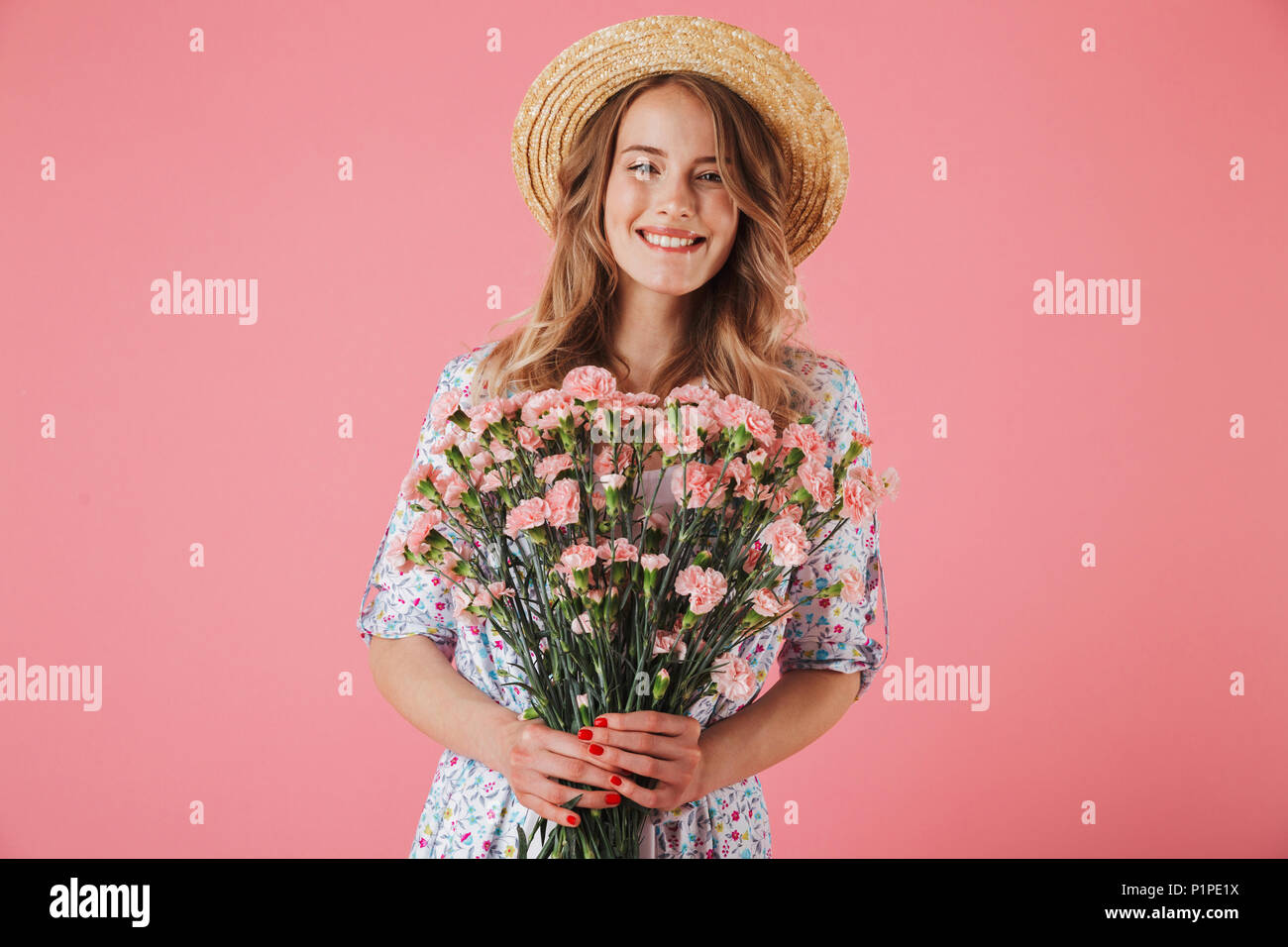 Portrait of a smiling young woman in summer dress and straw hat holding ...