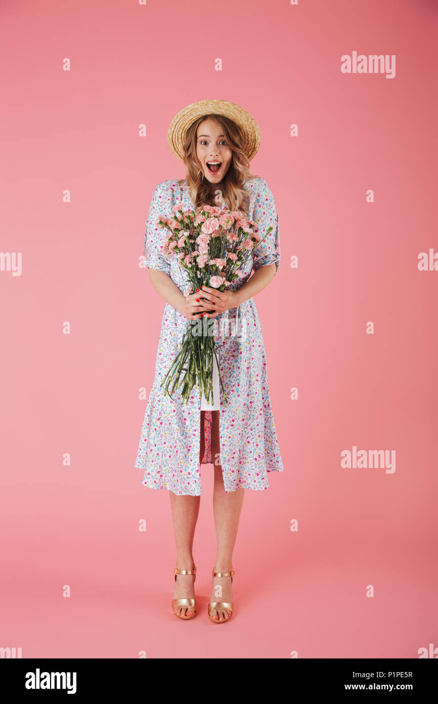 Full length portrait of a joyful young woman in summer dress and straw ...