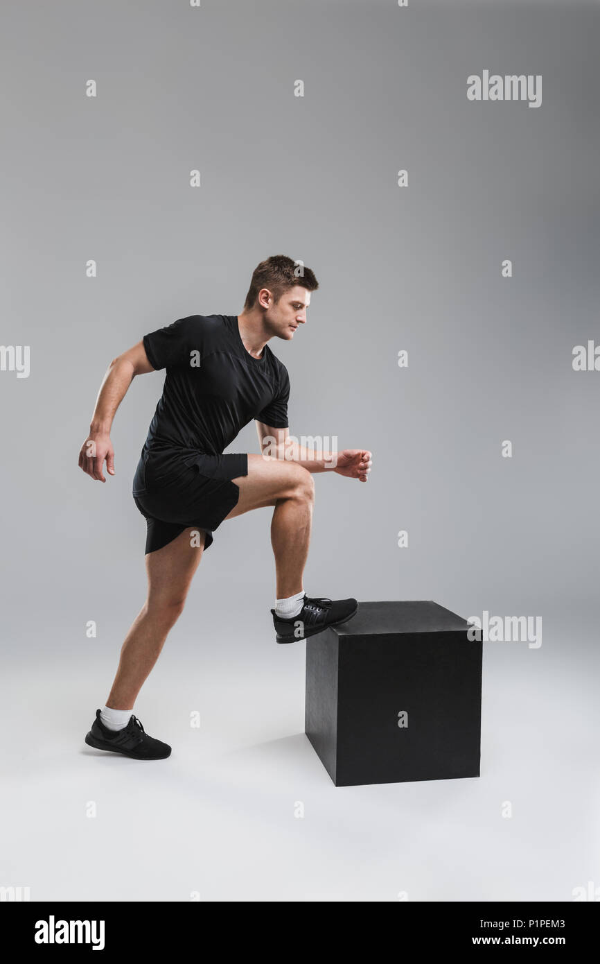 Full length portrait of a strong young sportsman stepping on a block isolated over gray background Stock Photo