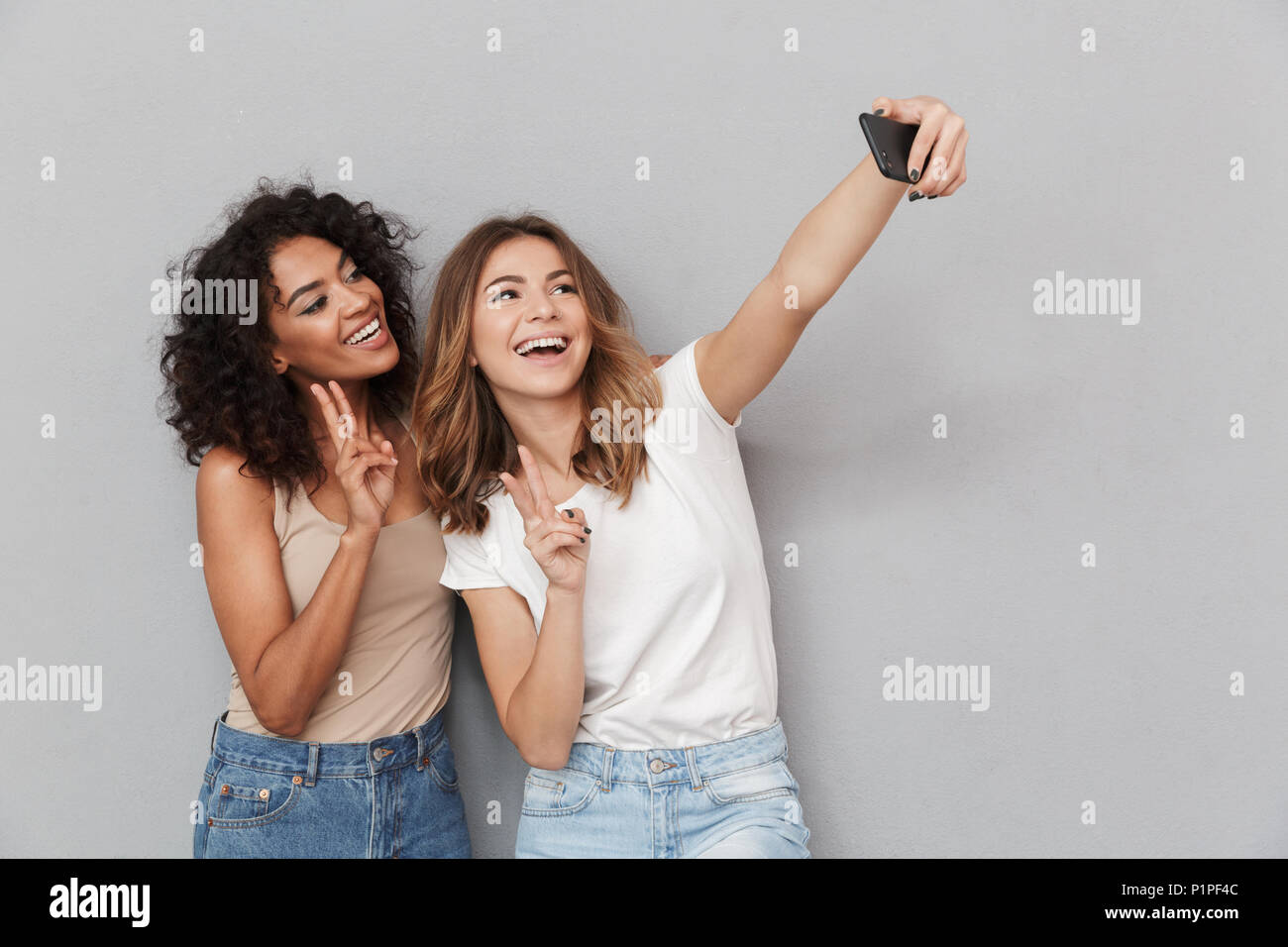 Portrait of two happy young women taking selfie with mobile phone ...