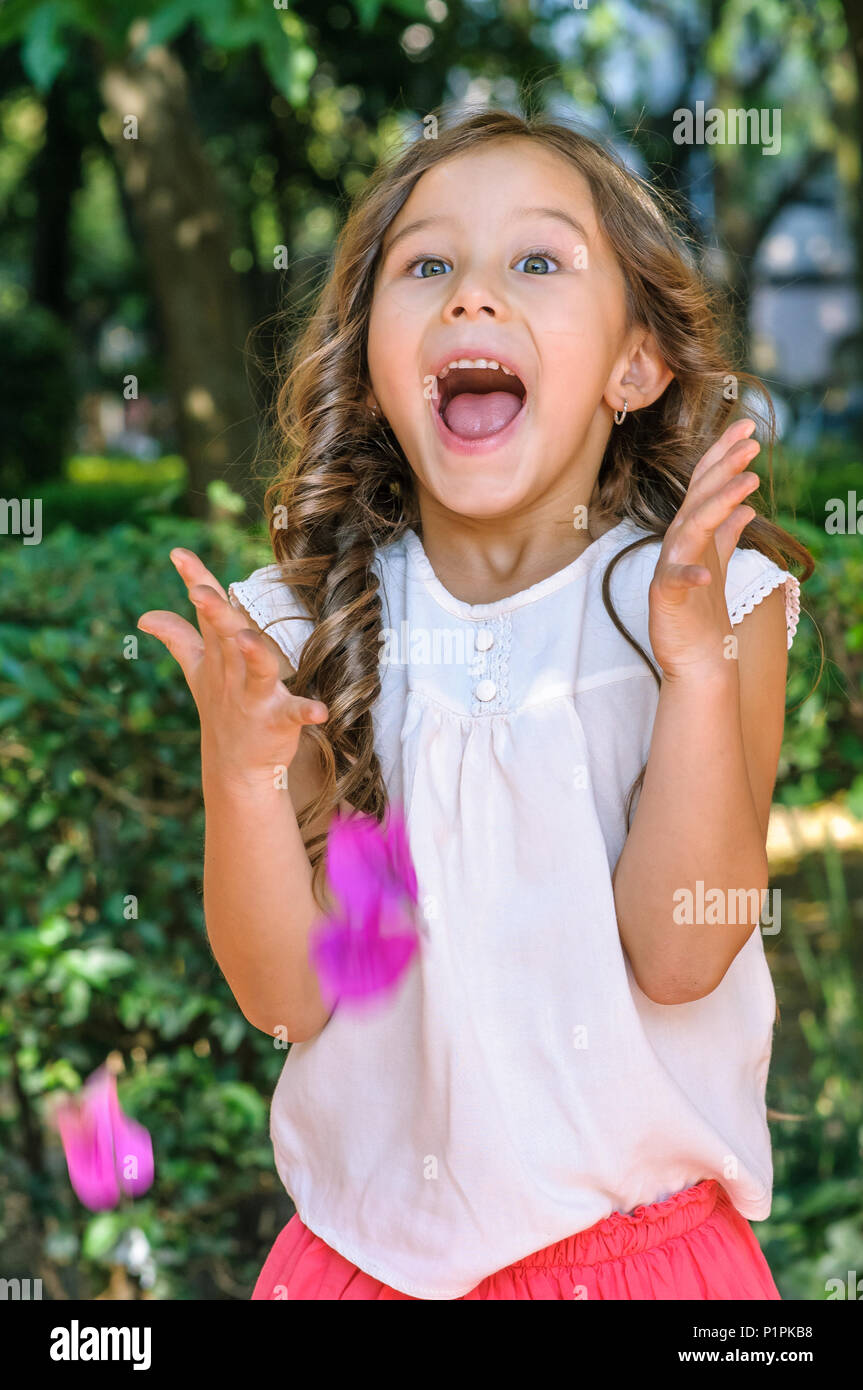 Cute five years old little girl with blue eyes and blond hair showing happiness and surprised on her face with a park as background Stock Photo