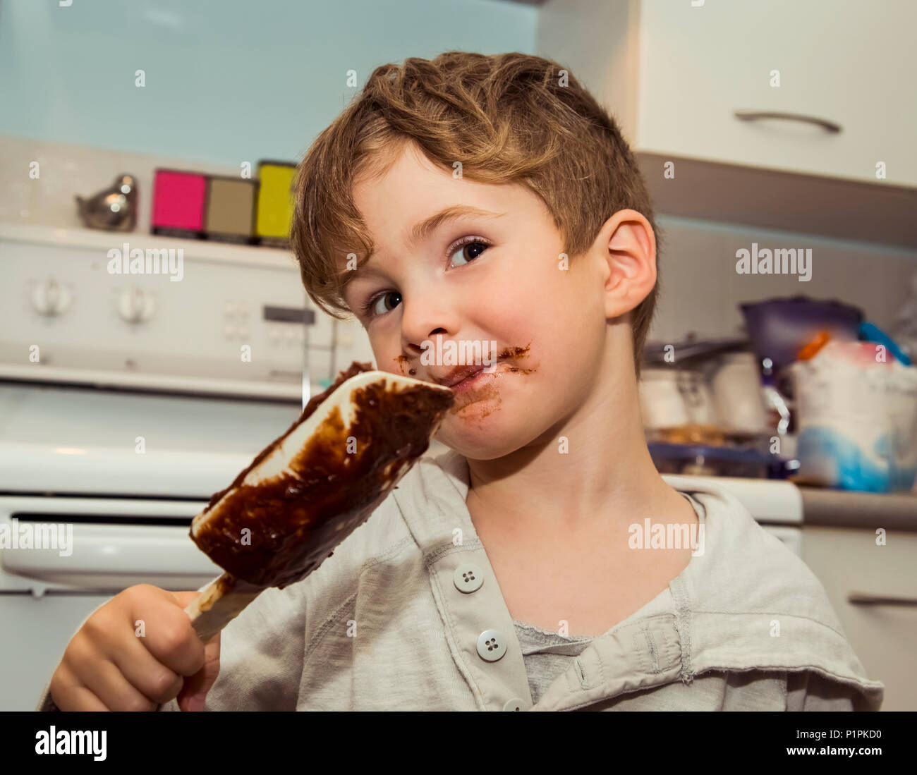 A grinning young boy with a messy face licks the chocolate from the spatula after making fudge; Langley, British Columbia, Canada Stock Photo