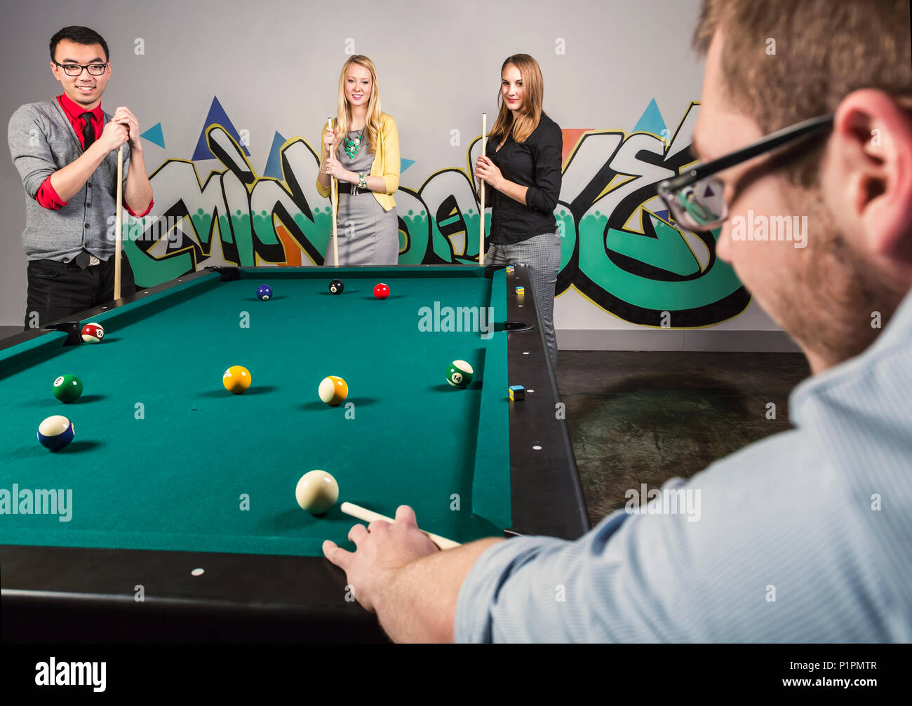 A group of young millennial business professionals playing a game of pool together on a work break; Sherwood Park, Alberta, Canada Stock Photo