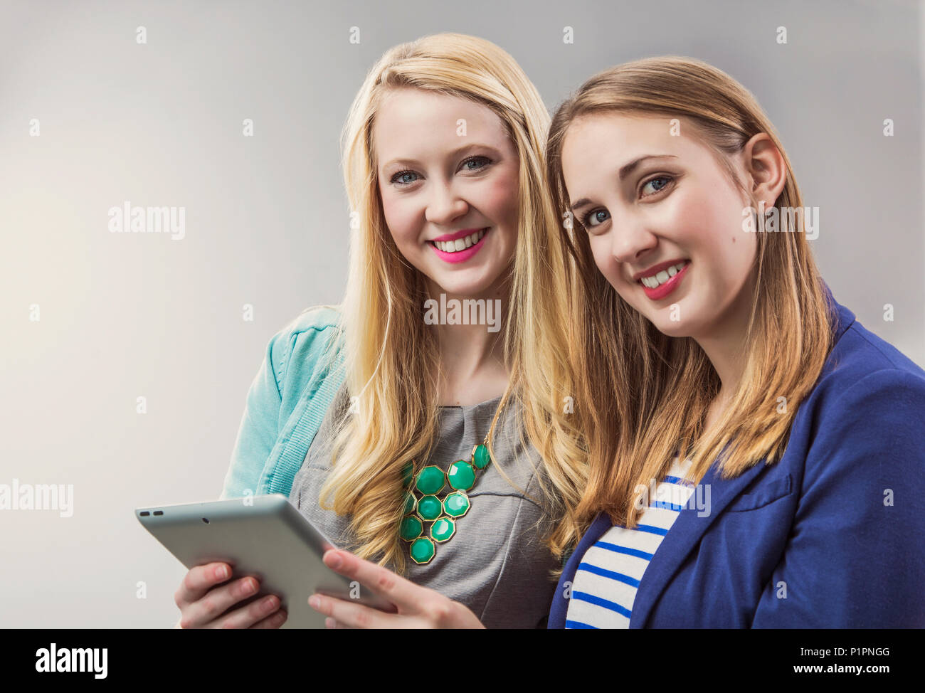 Two beautiful young women who are millennial business professionals working together using a tablet and posing for the camera at their workplace Stock Photo