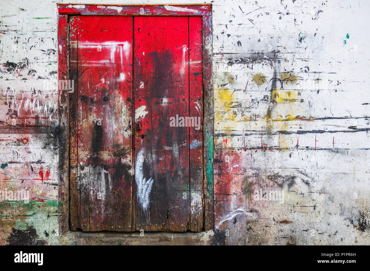 Red wooden doors and wall splattered with multiple paint colours; Nicaragua Stock Photo