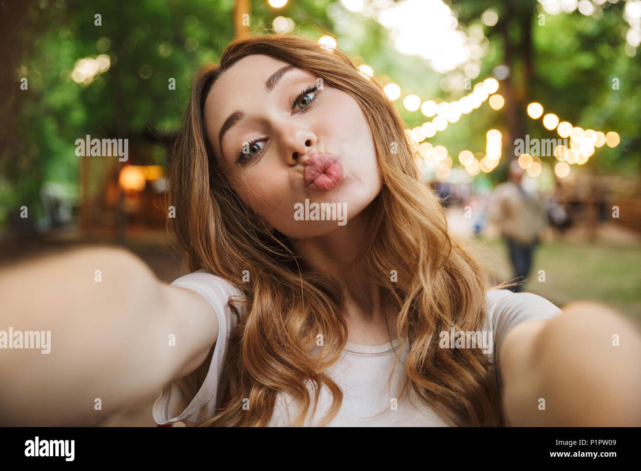 Close up of pretty young girl taking a selfie with outstretched hand while standing at the park Stock Photo
