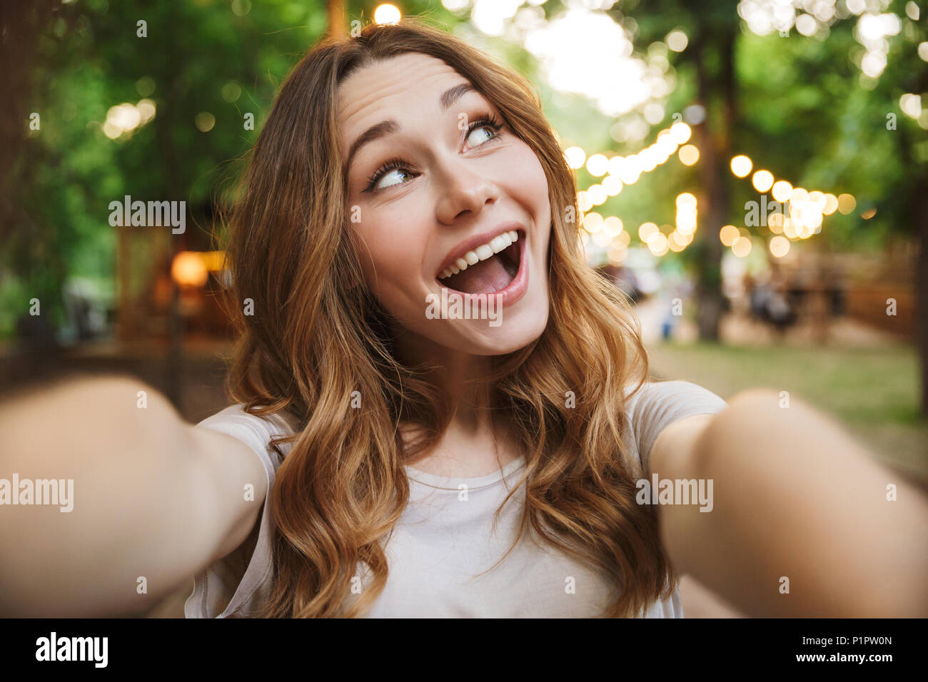 Close up of cute young girl taking a selfie with outstretched hand while standing at the park Stock Photo