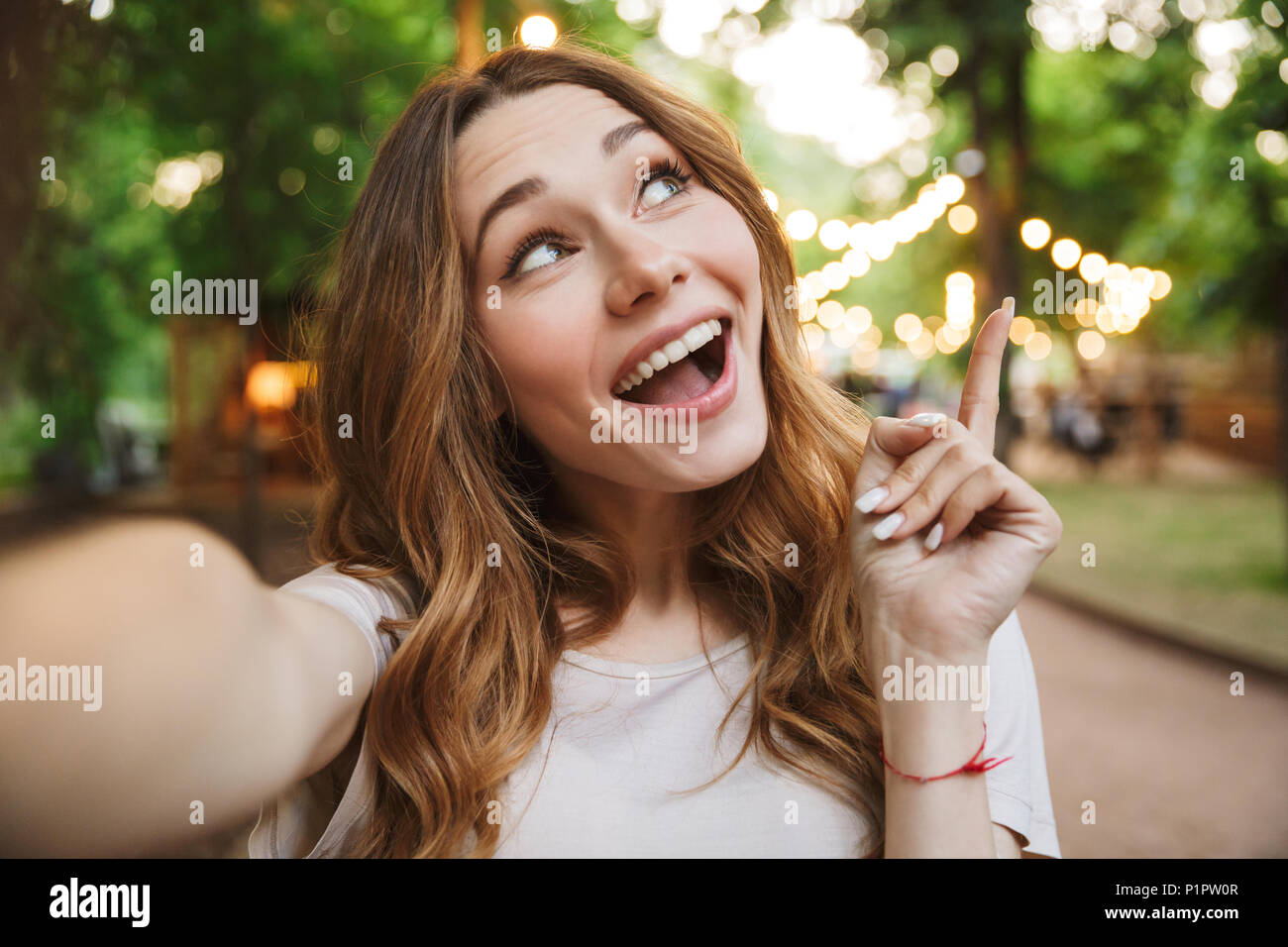 Close up of dreamy young girl taking a selfie with outstretched hand while standing at the park Stock Photo