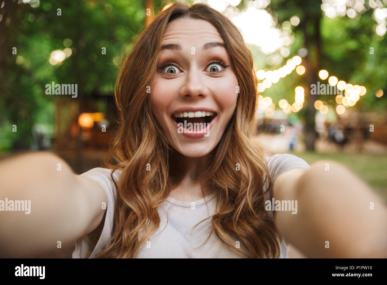 Close up of excited young girl taking a selfie with outstretched hand while standing at the park Stock Photo