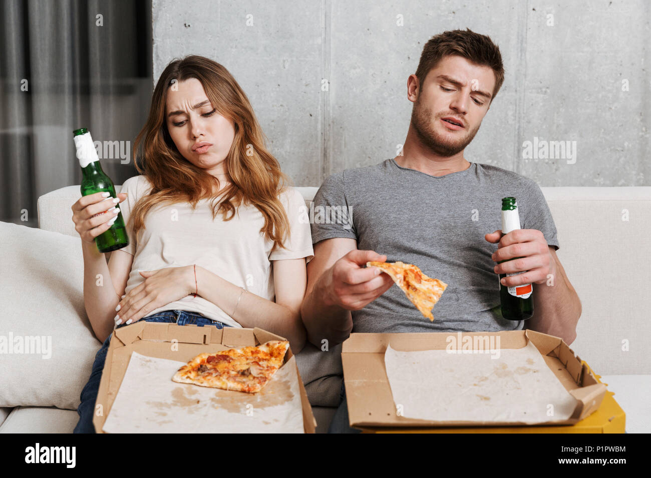 Sick couple ate too much pizza while sitting together on a couch at