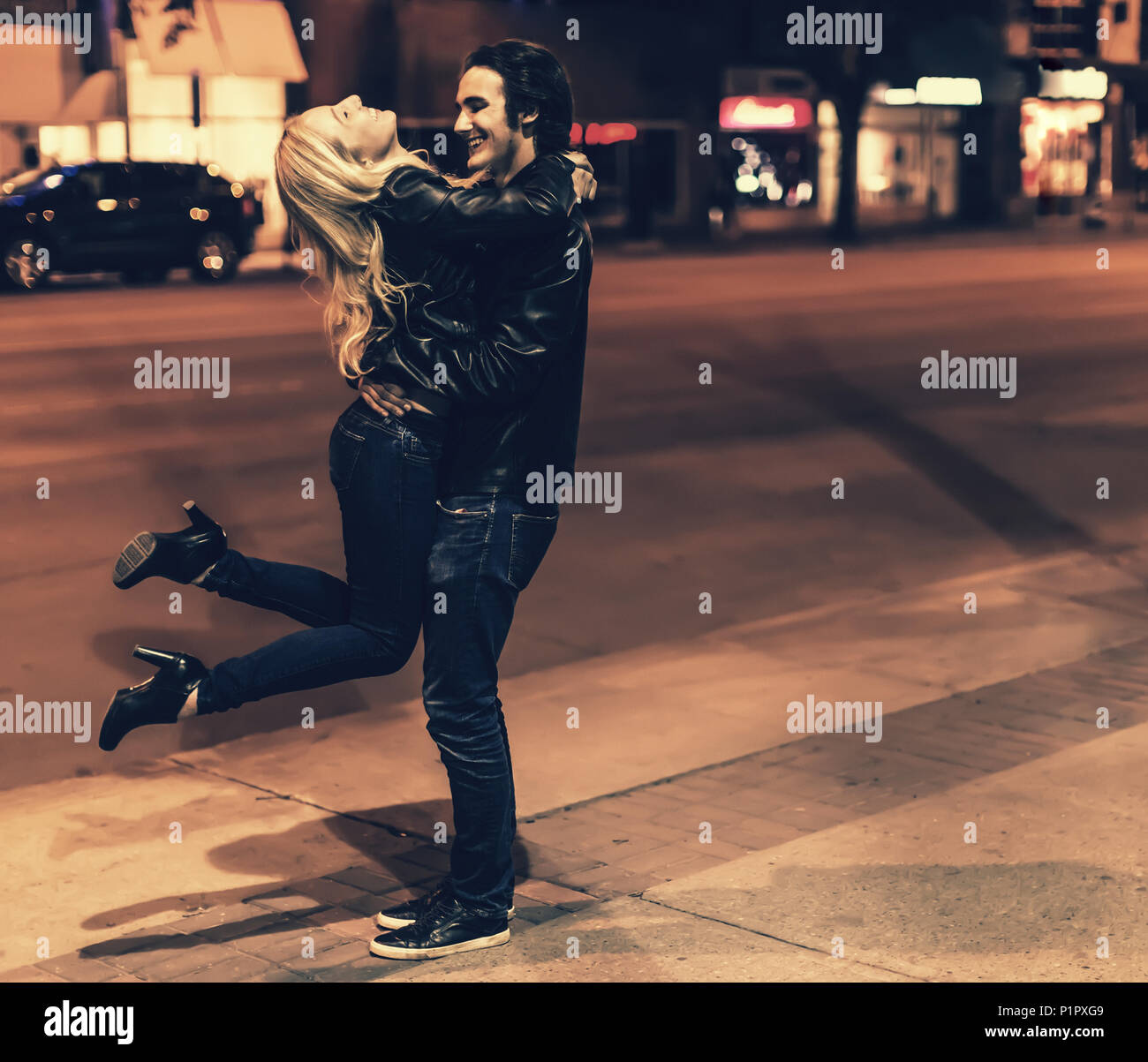 A young couple wearing black leather jackets being playful on a city sidewalk at night; Edmonton, Alberta, Canada Stock Photo