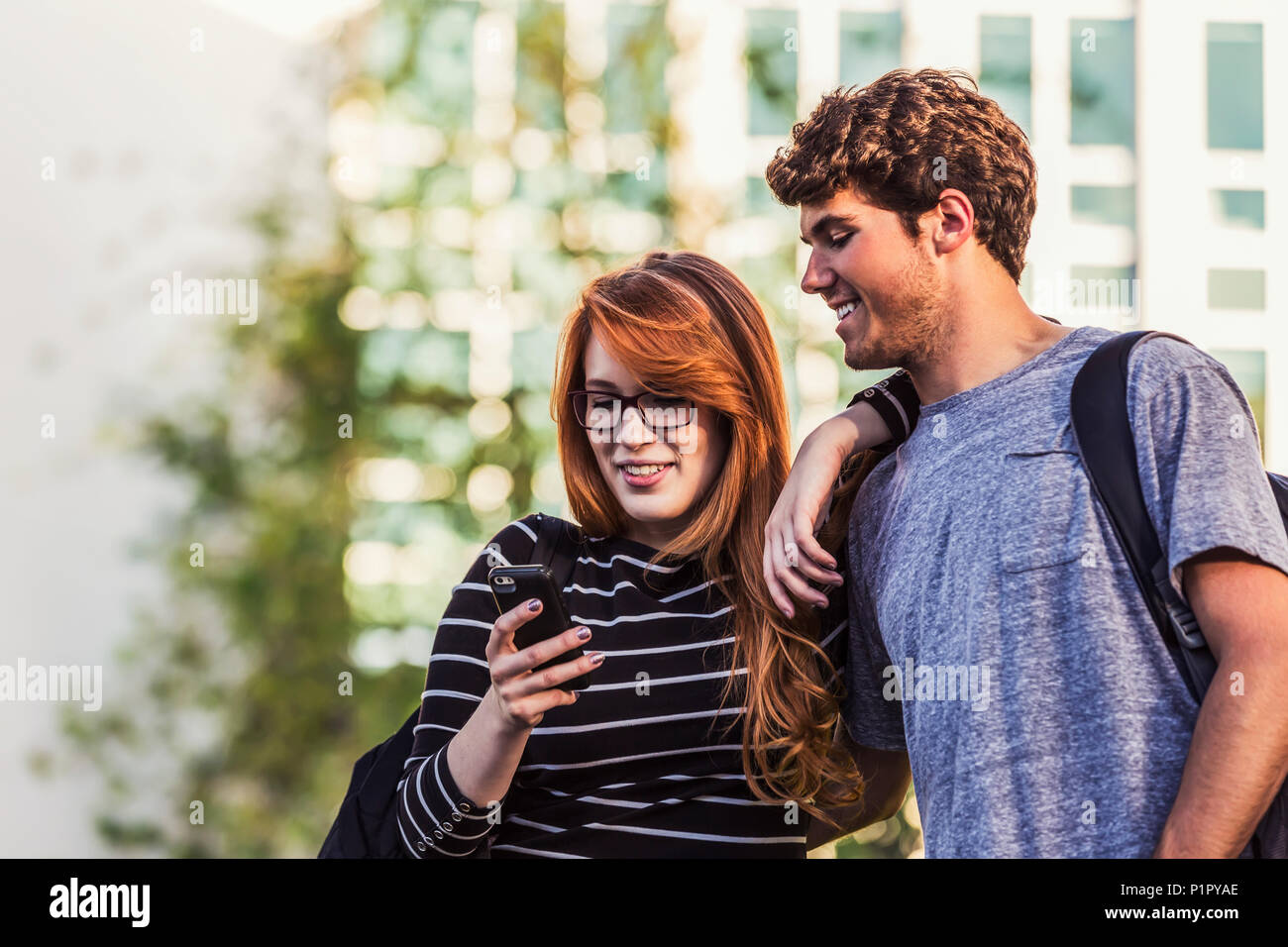 A young couple standing together and checking social media on a smart phone while walking through a university campus; Edmonton, Alberta, Canada Stock Photo
