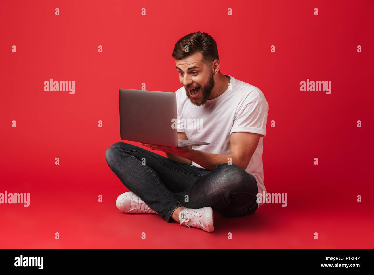 Photo Of Happy Excited Man In T Shirt And Jeans Sitting On Floor And Screaming Like Lucky Guy Or