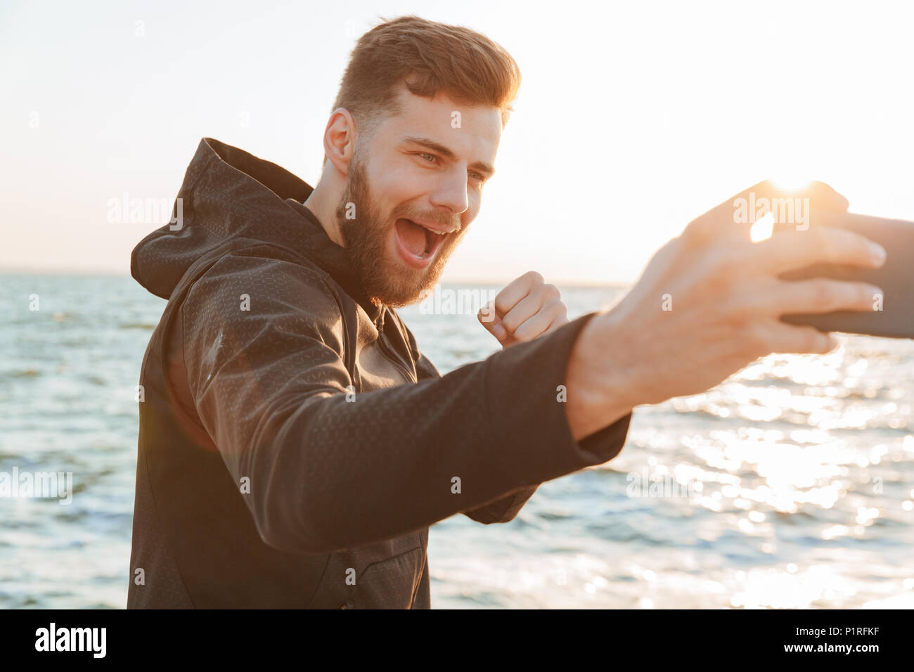 Happy young sportsman taking selfie with mobile phone while standing at