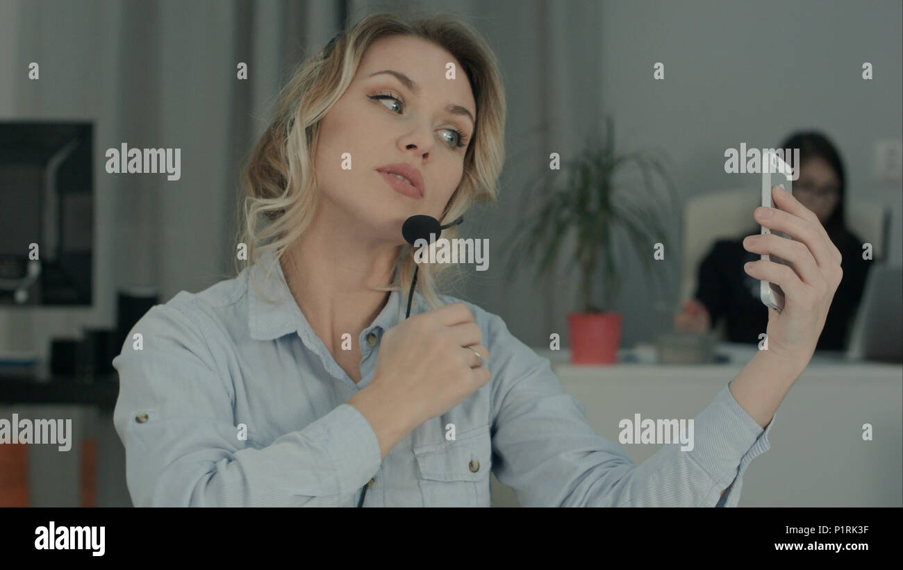 Young office worker in headset taking selfies on her phone Stock Photo