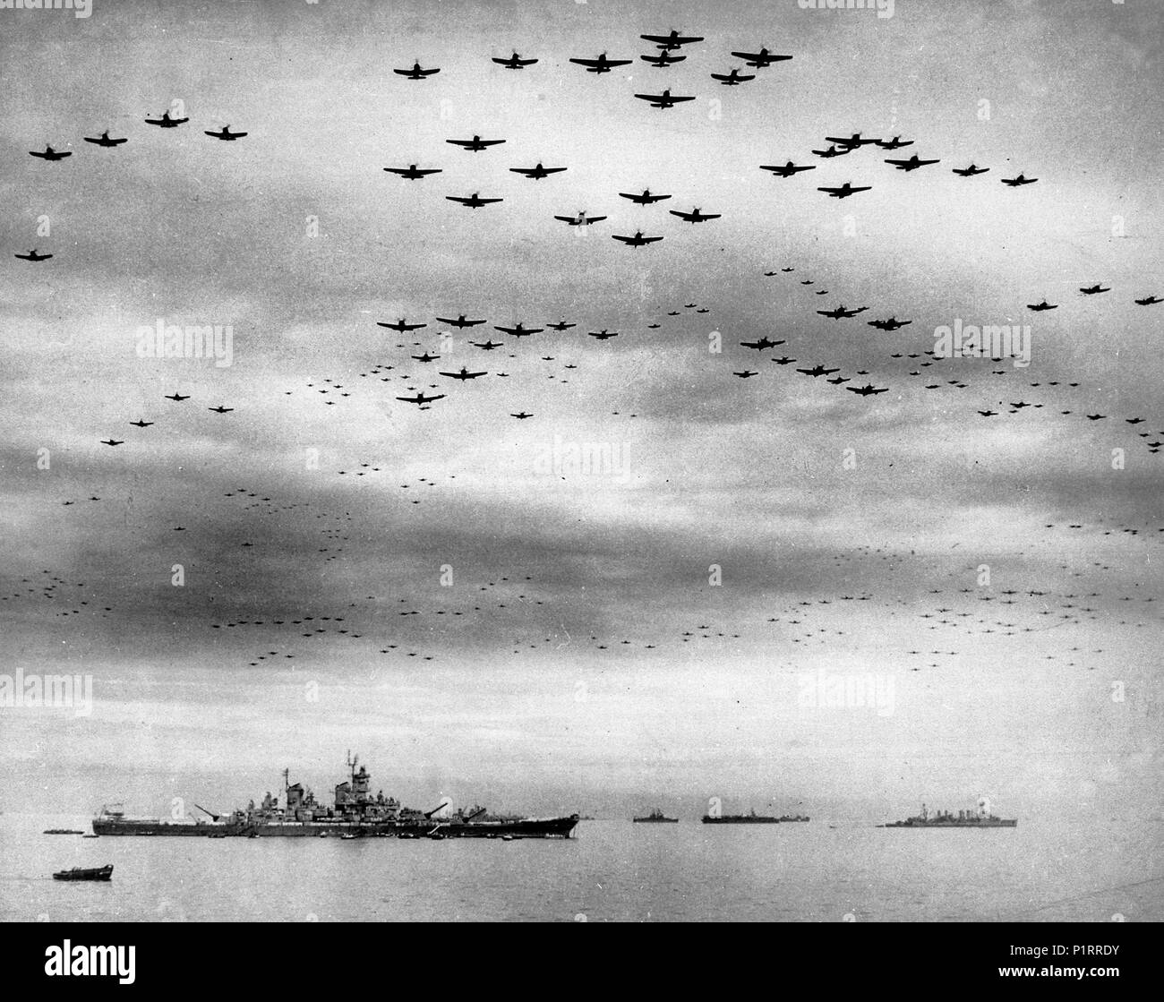 Surrender of Japan, 2 September 1945: U.S. Navy carrier planes fly in formation over the U.S. and British fleets in Tokyo Bay during surrender ceremonies. The battleship USS Missouri (BB-63), where the ceremonies took place, is at left. The light cruiser USS Detroit (CL-8) is in the right distance. Aircraft include Grumman TBM Avenger, Grumman F6F Hellcat, Curtiss SB2C Helldiver and Vought F4U Corsair types. September 2, 1945 Stock Photo