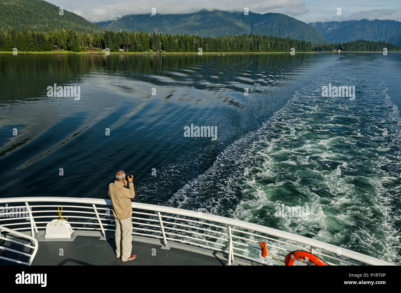 Tourist photographing Wrangell Narrows looking North toward Petersburg from stern of Alaska State Ferry, Southeast Alaska Stock Photo