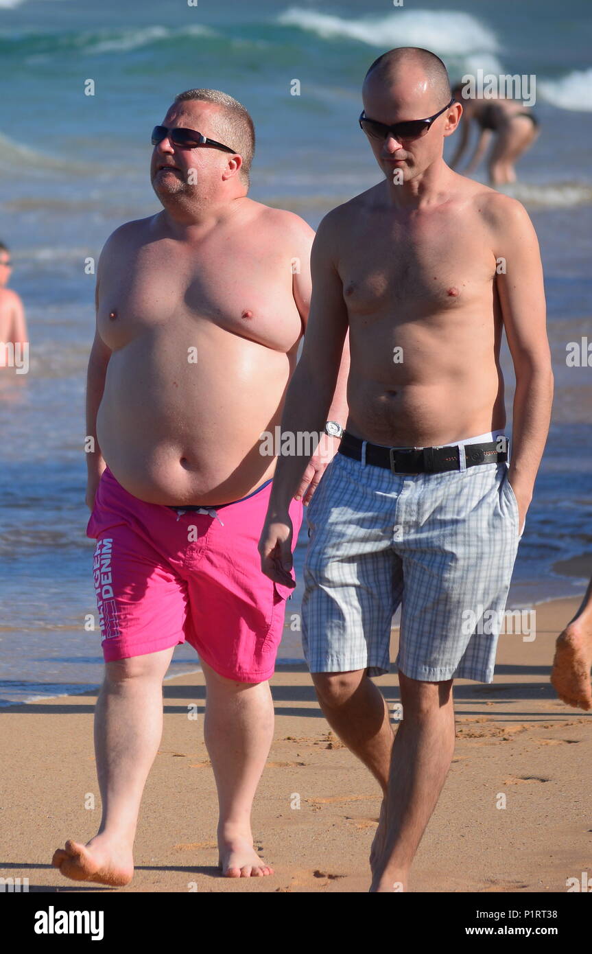 An overweight, obese man and a skinny man walk on the beach Stock Photo