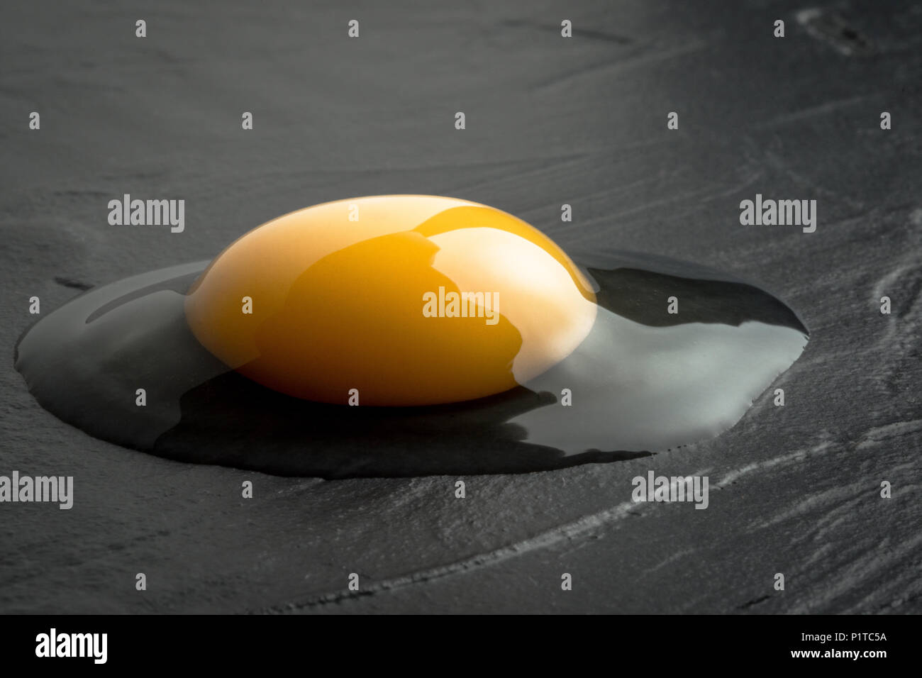 Broken Raw Egg Yolk on Dark Stone Background Stock Photo