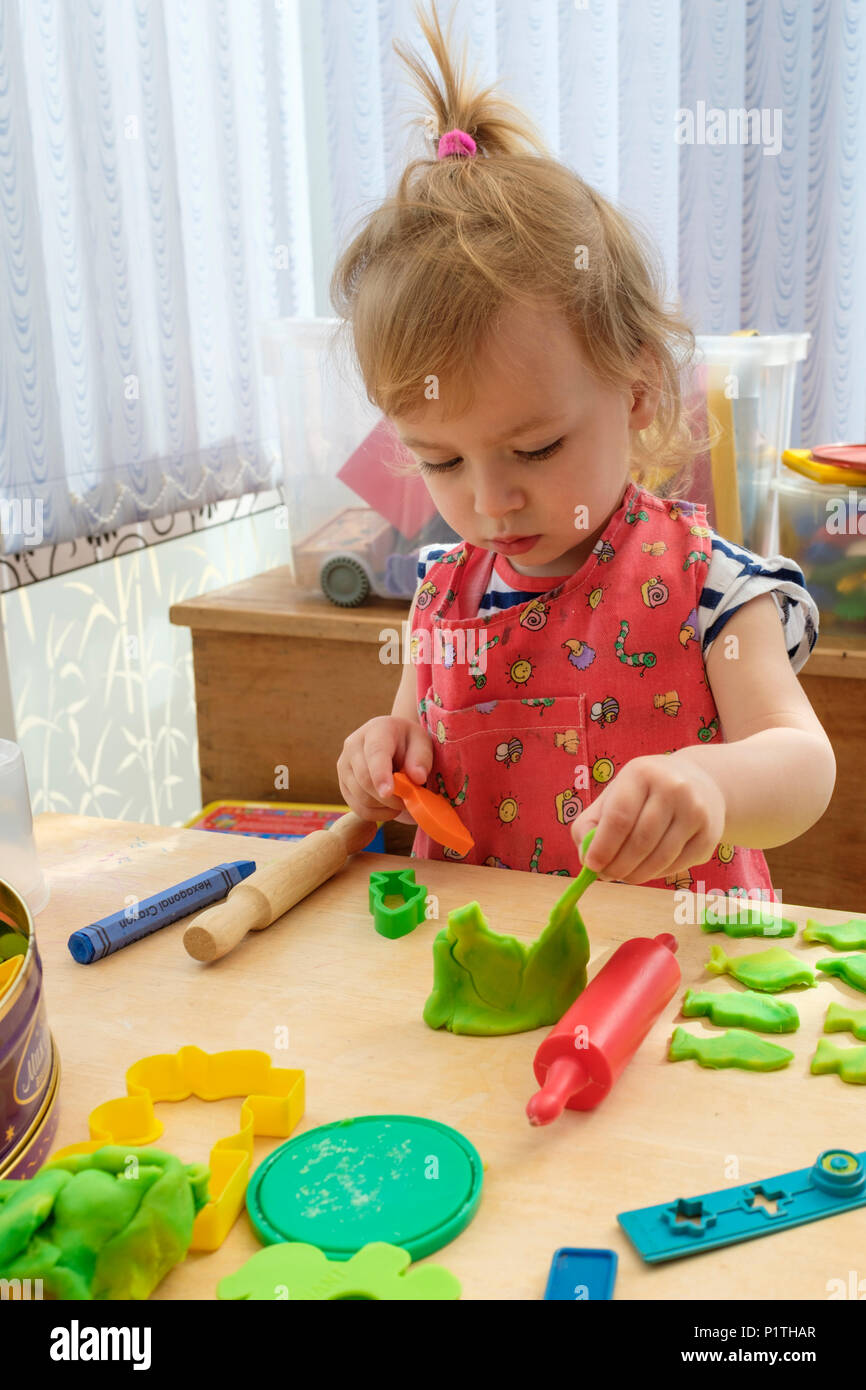 Learning through play. Happy young two year old girl playing and cutting out modelling dough clay. Stock Photo