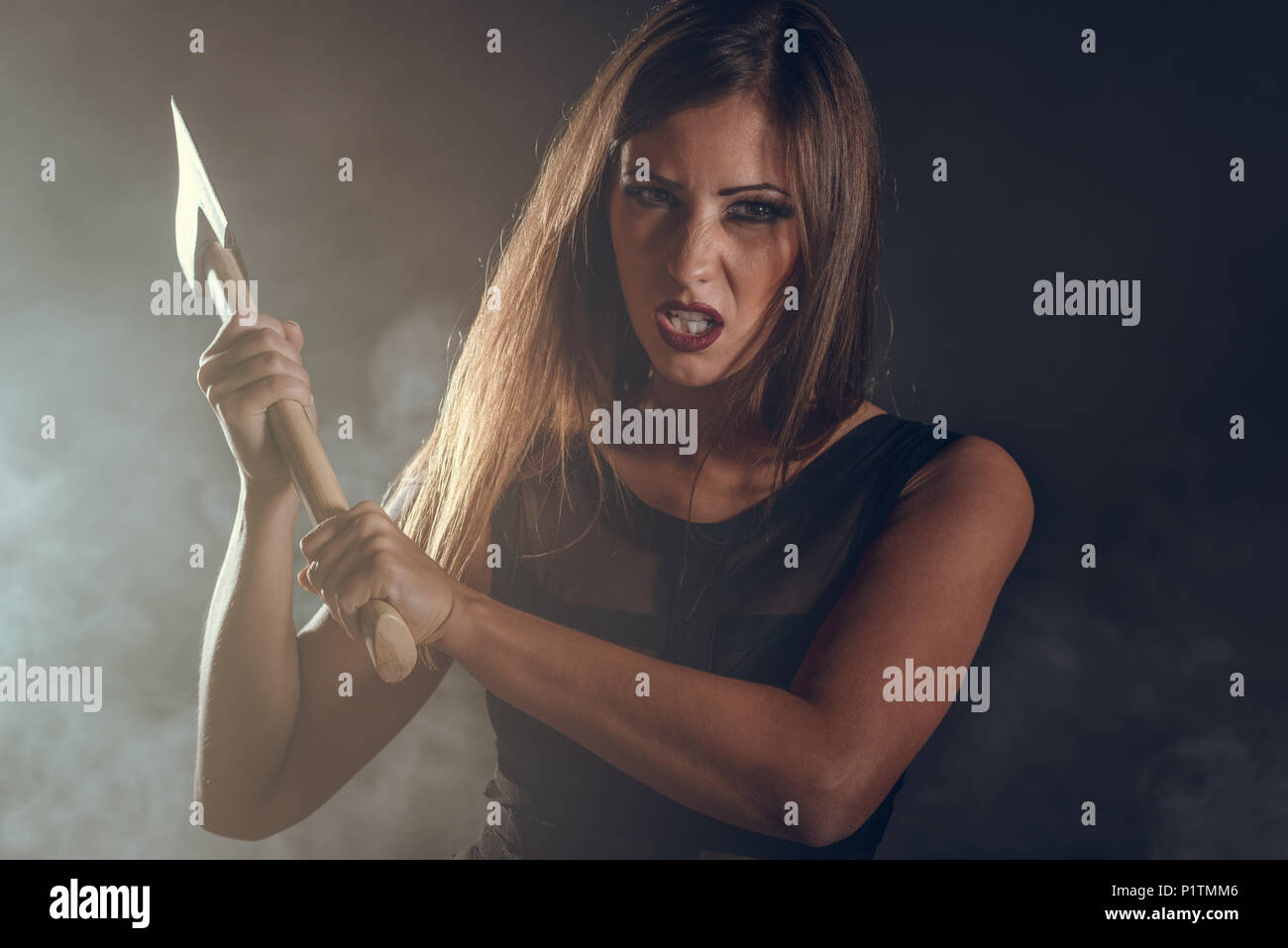 Beautiful dangerous girl with rusty axe want to revenge for violence she experience. Looking at camera. Stock Photo