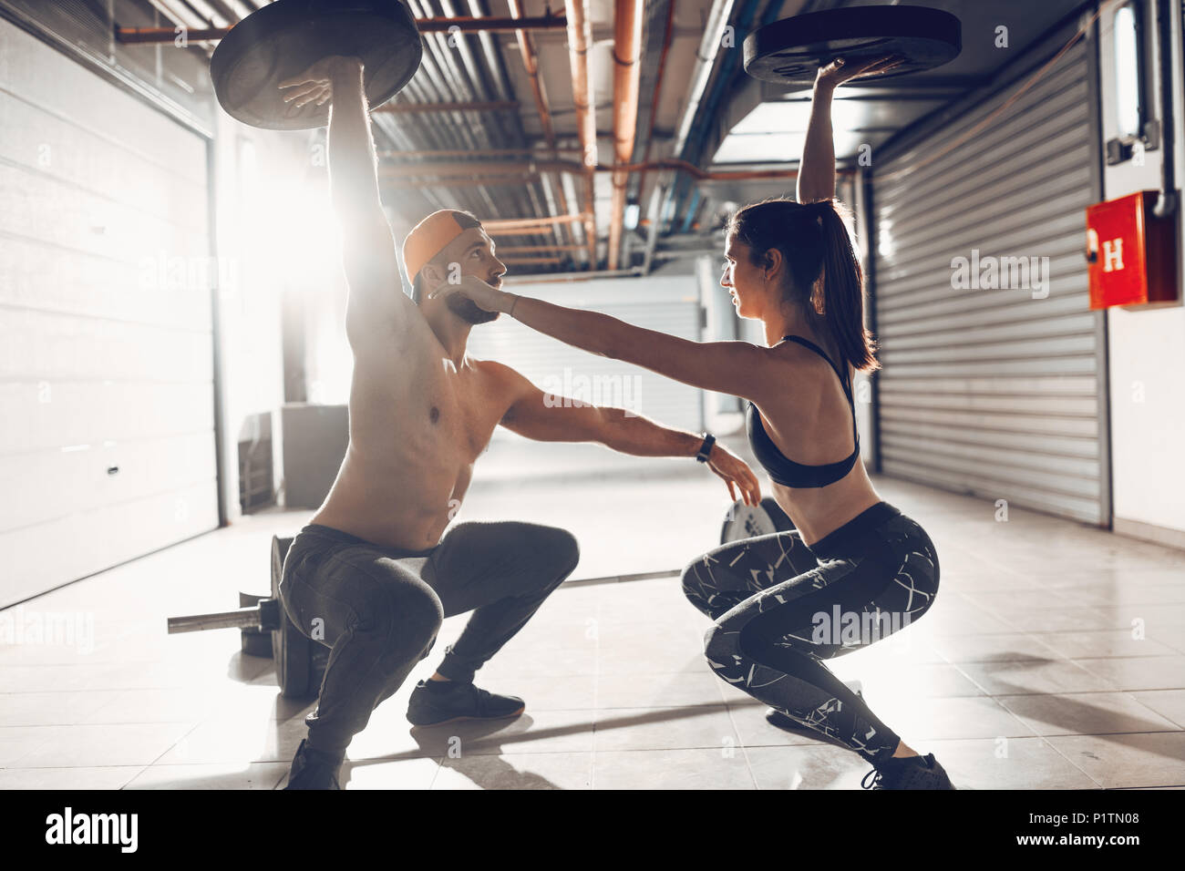 Young muscular couple doing hard plank exercise with plate weights on cross training at the garage gym. Stock Photo