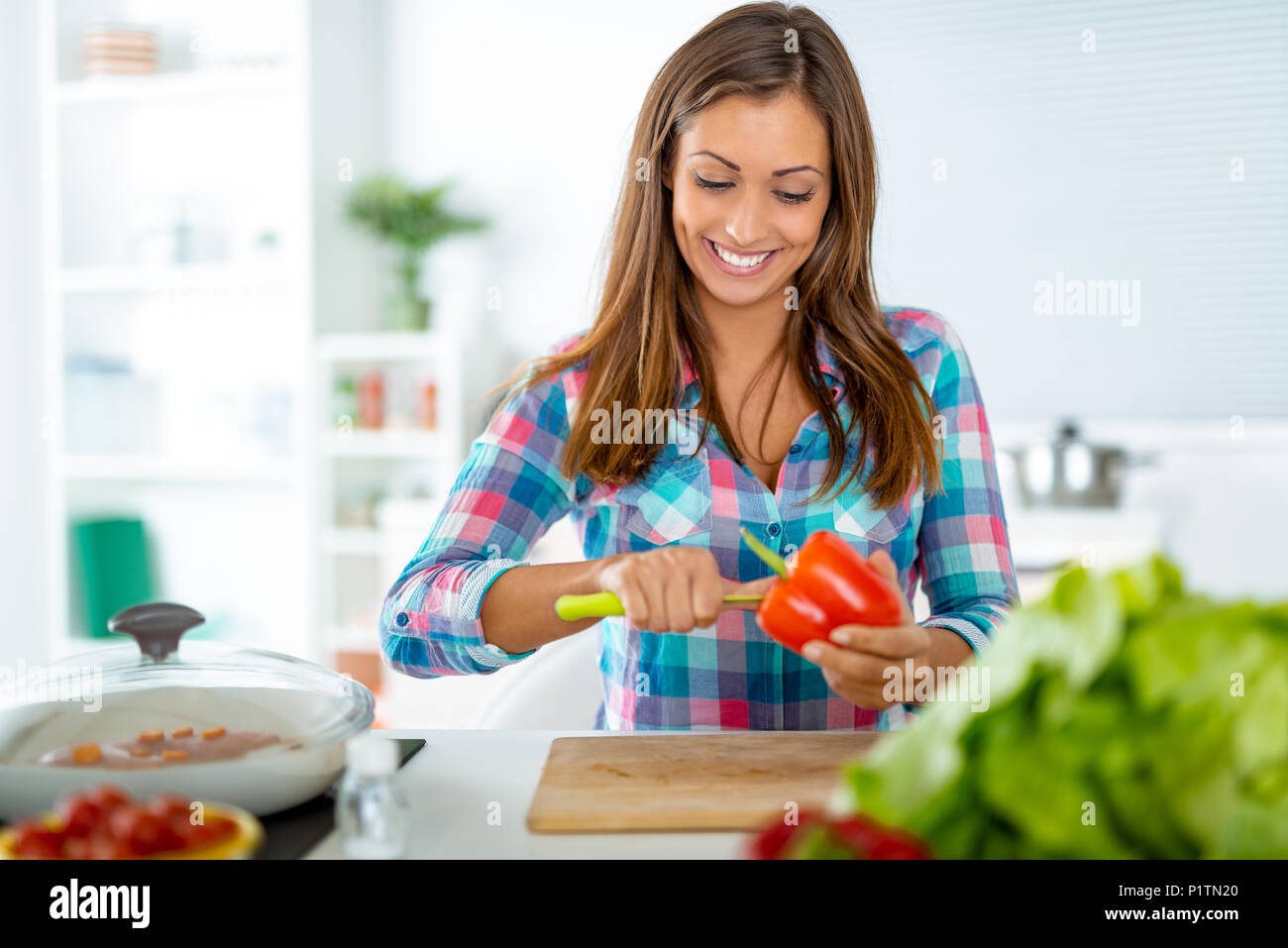 Beautiful young woman making healthy meal in the domestic kitchen. She prepares pepper for filling. Stock Photo