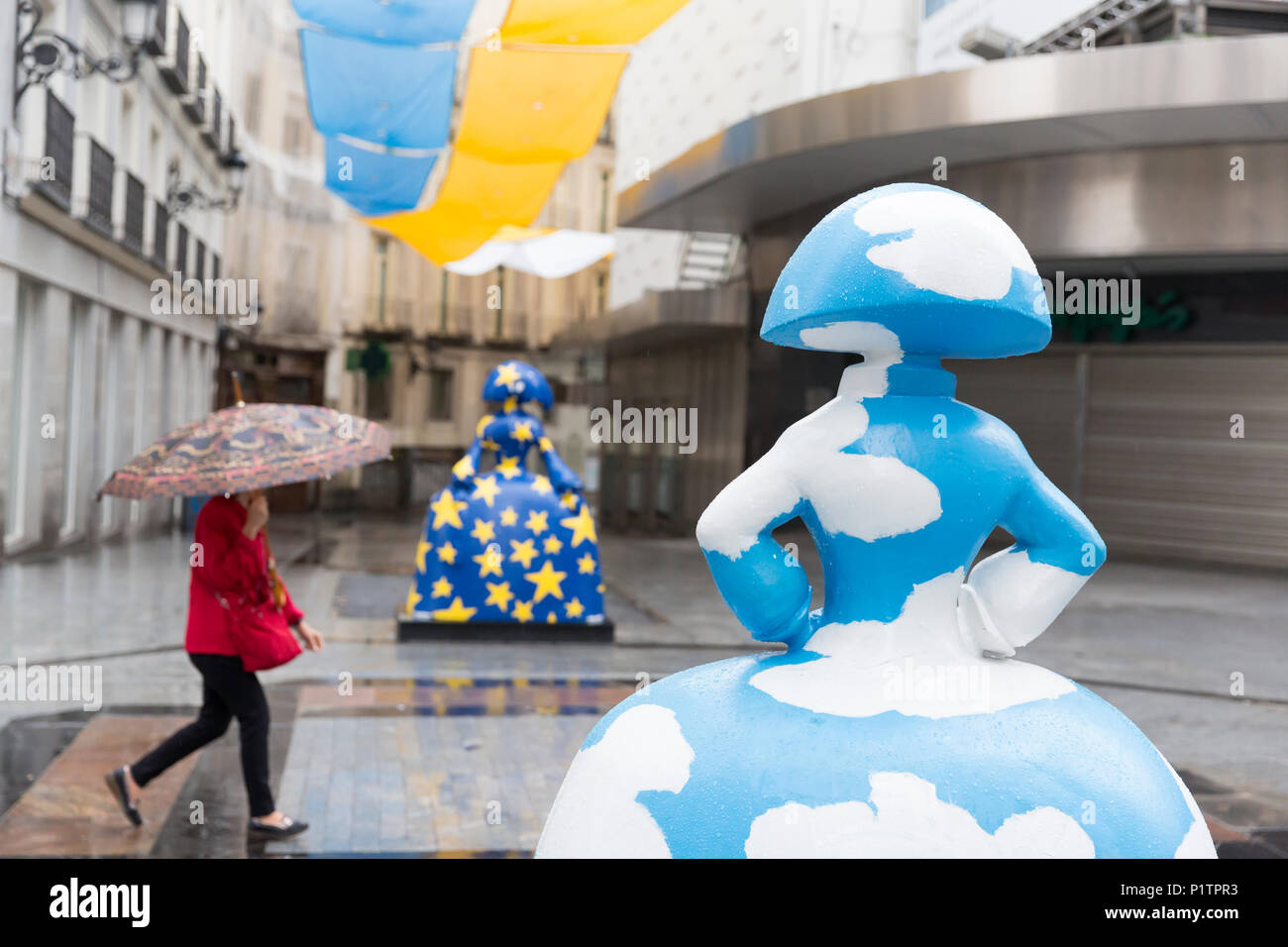 Madrid, Spain: Woman with an umbrella passes two 'Menina' sculptures along Calle de Preciados. The sculptures are part of the 'Meninas Madrid Gallery' Stock Photo