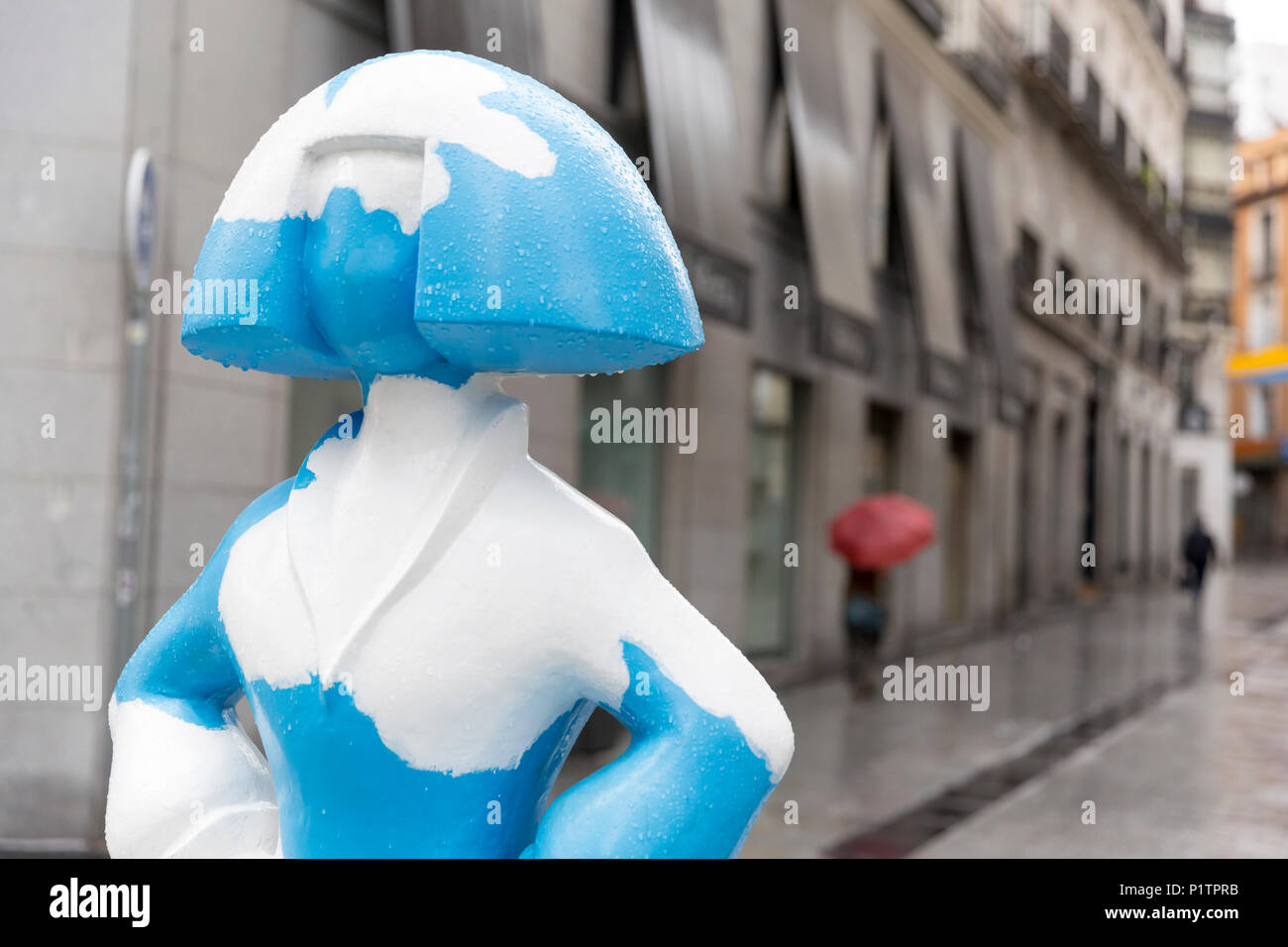 Madrid, Spain: A woman with an umbrella passes a 'Menina' sculpture along Calle de Tetuán. The sculpture is part of the 'Meninas Madrid Gallery' in tr Stock Photo