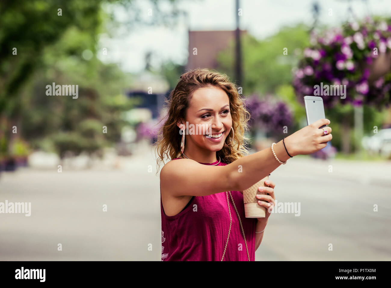 A young beautiful woman takes a self-portrait on a cell phone on a street near a university campus; Edmonton, Alberta, Canada Stock Photo
