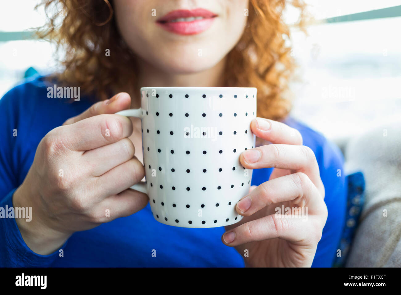 Woman with red, curly hair holding a polka dotted mug; Surrey, British Columbia, Canada Stock Photo