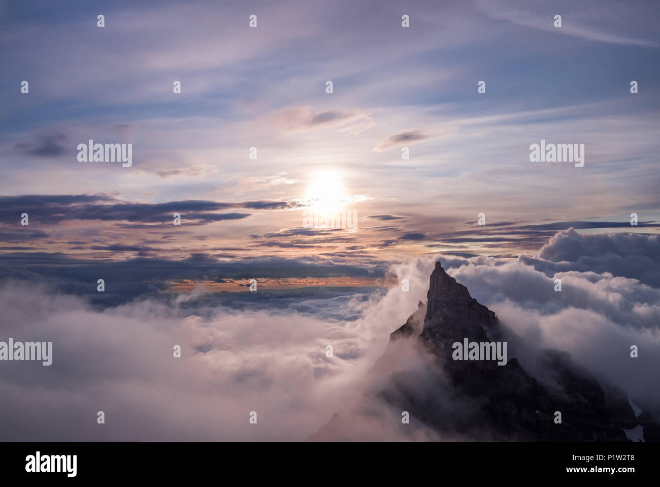 Mountain top peeks above the clouds, illuminated by the sun just after sunrise Stock Photo