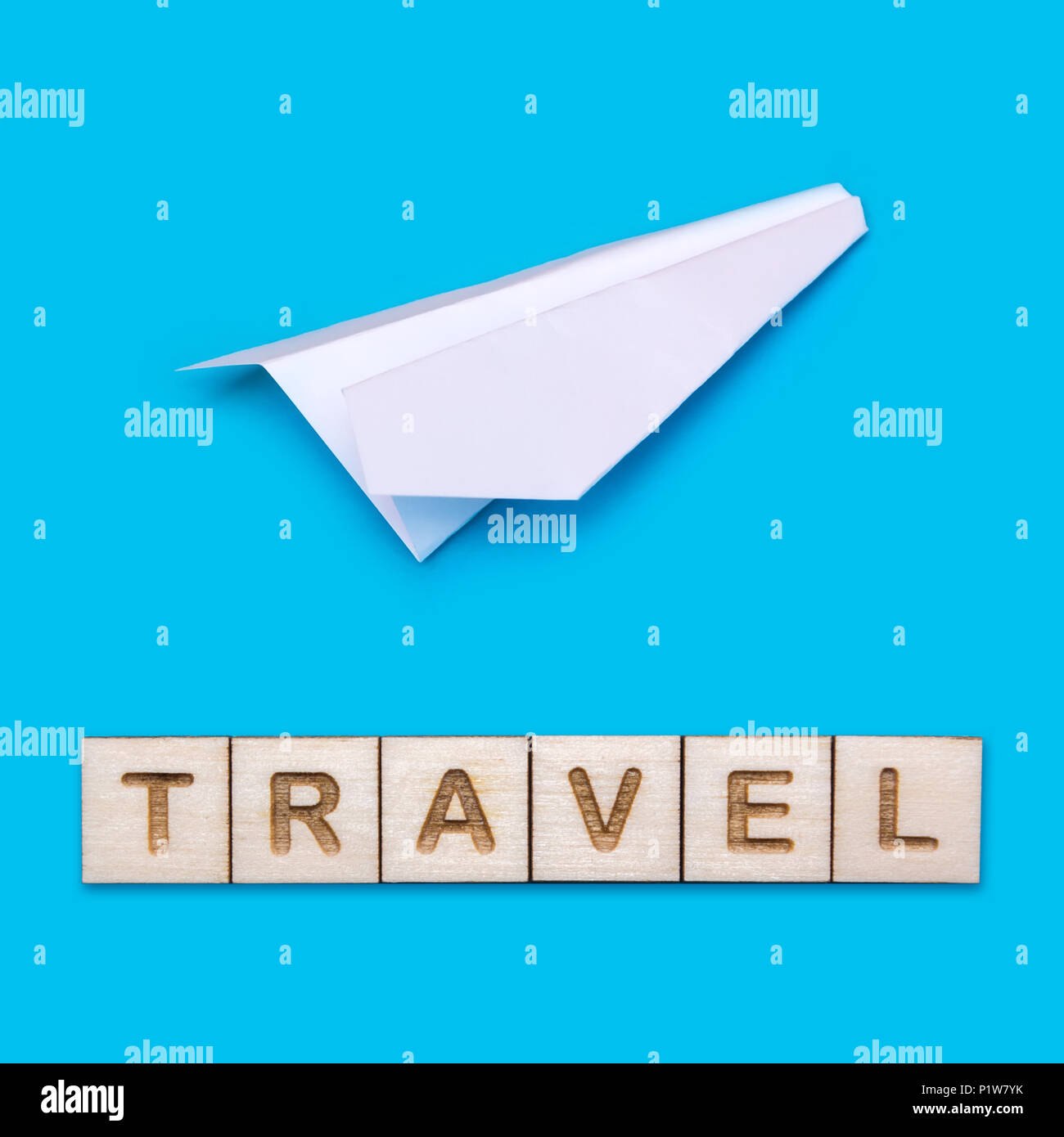 Concept on the theme of travel. White origami plane on a blue background. The word Travel is laid out of wooden blocks. Stock Photo
