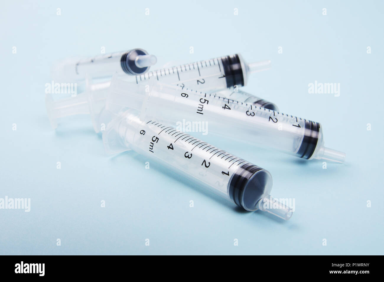 a stack of clear medical plastic syringes piled on top of each other neat and clean on a light blue background used for both human and animal purpose Stock Photo