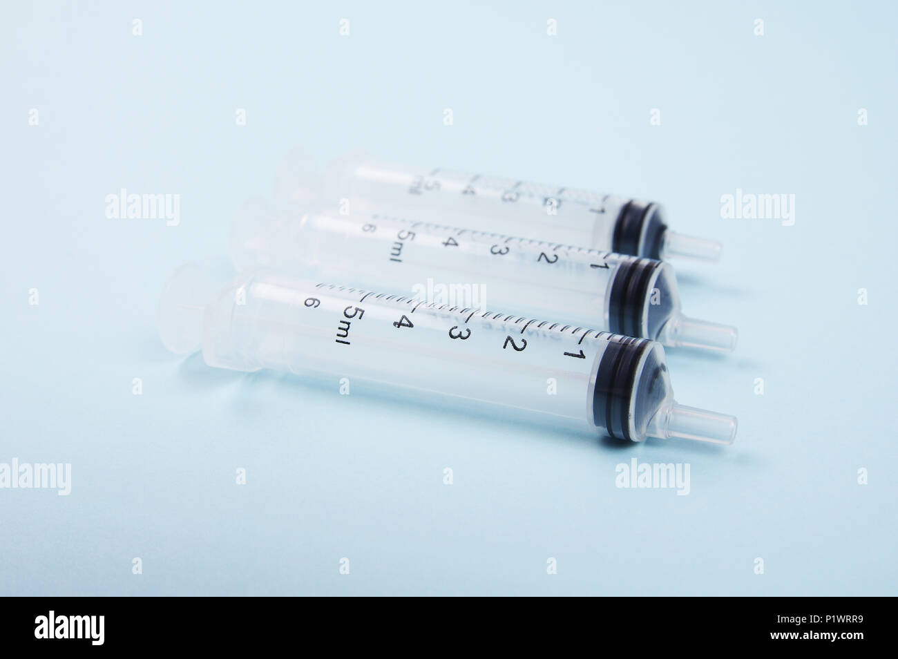three clear plastic medical syringes in a neat row on a light blue background Stock Photo