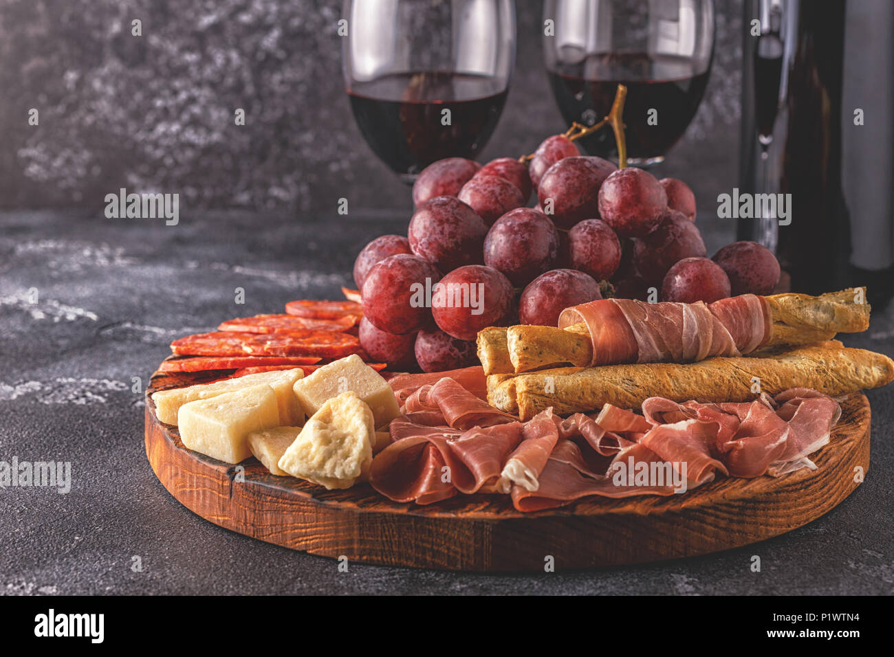 Prosciutto, sausage, wine, grape, parmesan on dark table, selective focus. Stock Photo