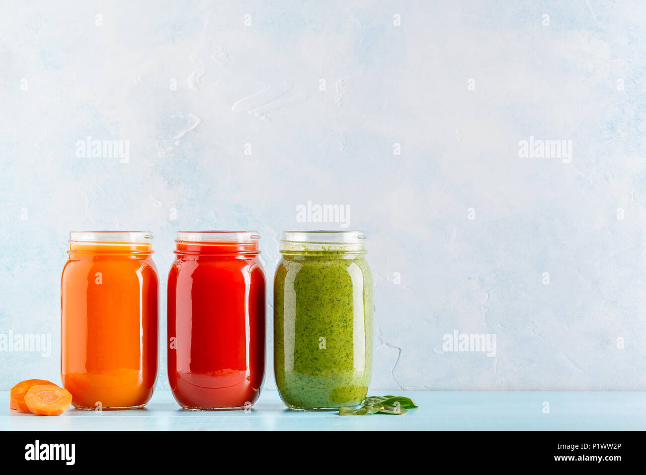 Orange/green/red colored smoothies / juice in a jar on a blue background. Stock Photo