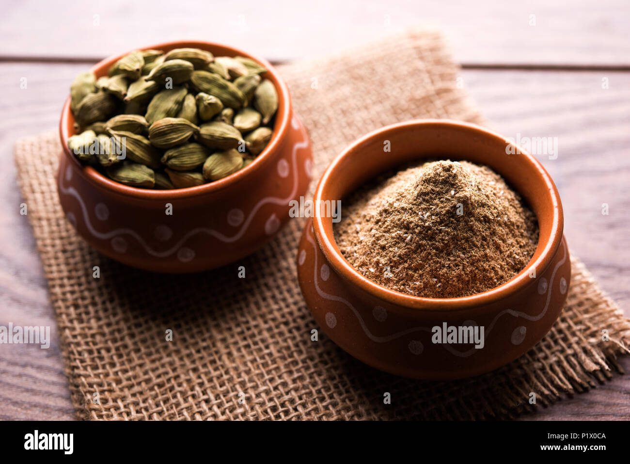 elaichi or Cardamom powder in bowl or heap over moody background with pods. selective focus Stock Photo
