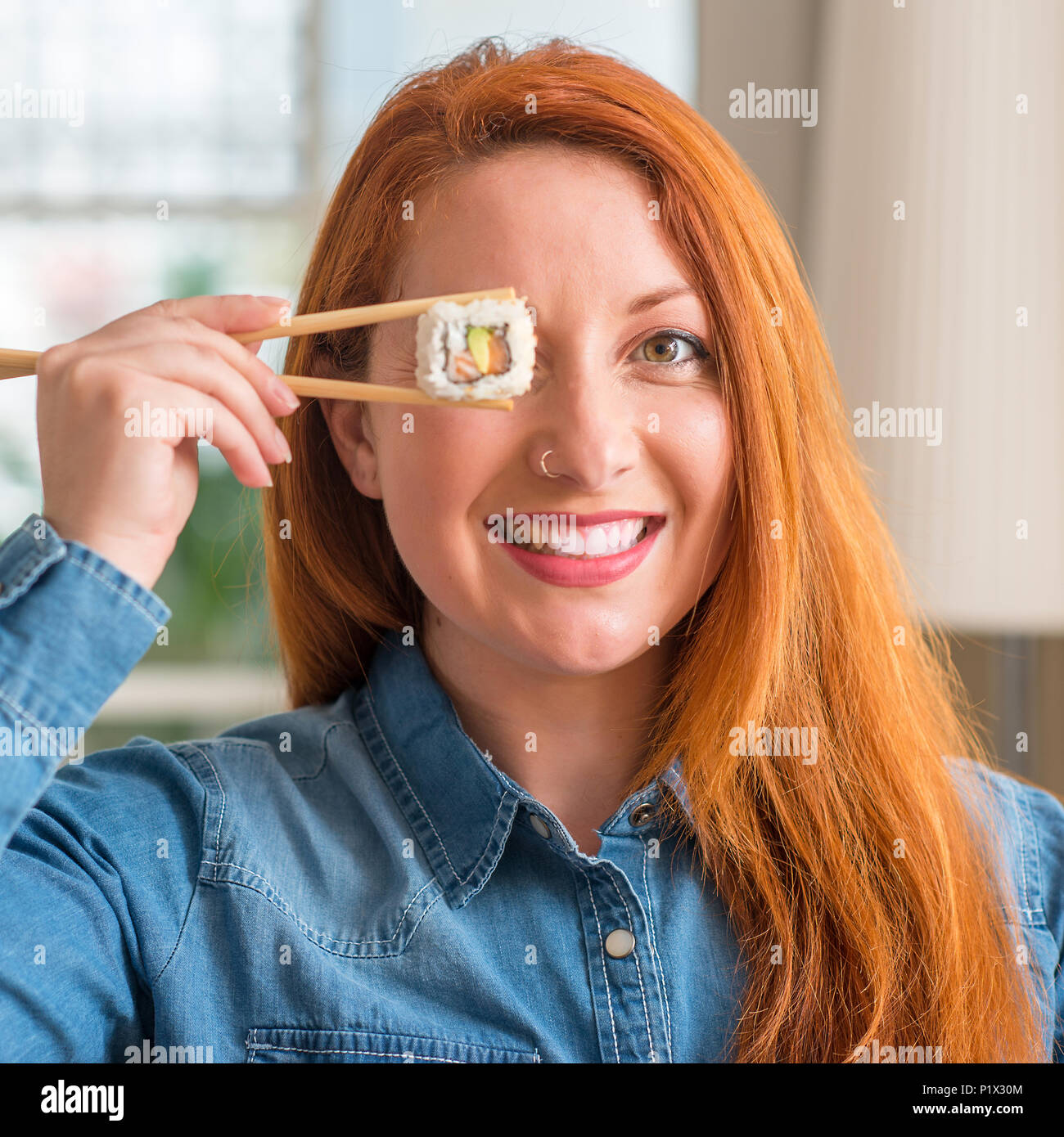 Redhead woman eating sushi using chopsticks with a happy face standing and smiling with a